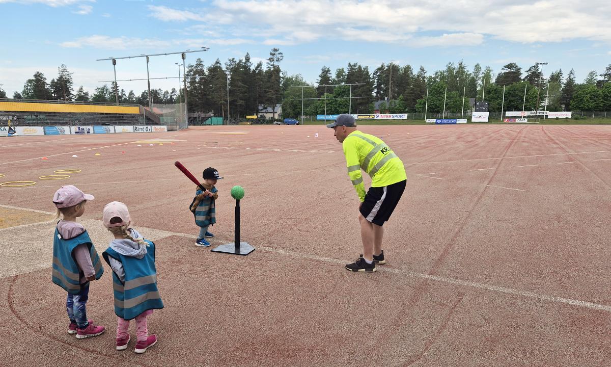 Työmaapäällikkö auttoi pesäpallopisteellä lapsia. 